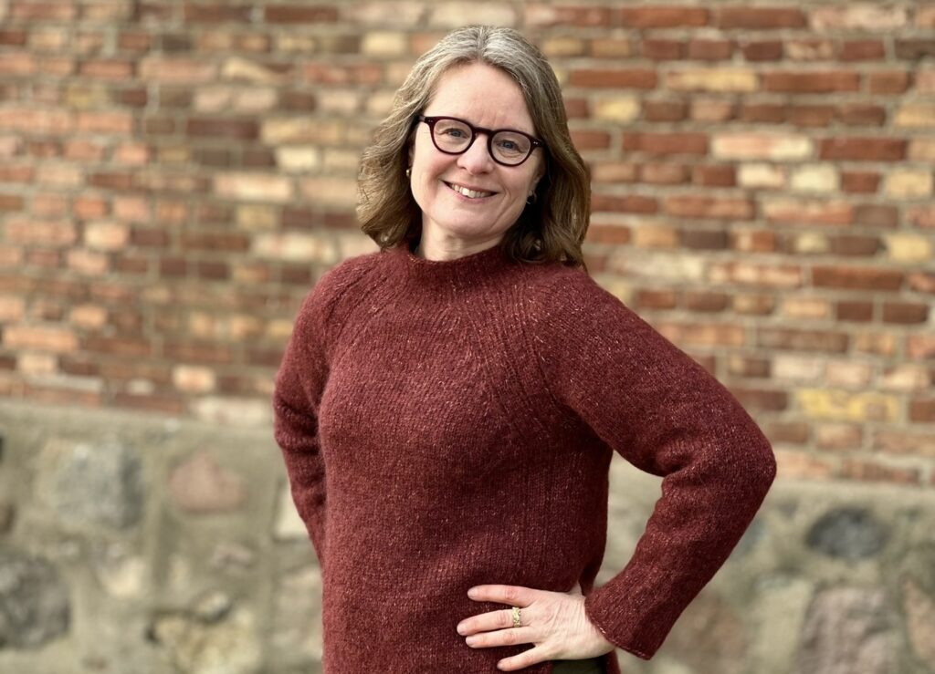 Susanne i röd tröja framför tegelvägg